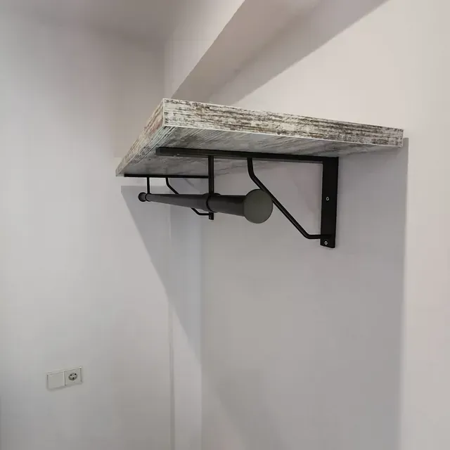 Un estante de madera con una varilla de metal unida a él está colgado en una pared blanca.