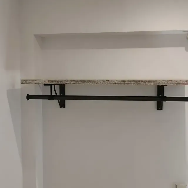 Un estante con una barandilla de metal adjunta está colgado en una pared blanca.