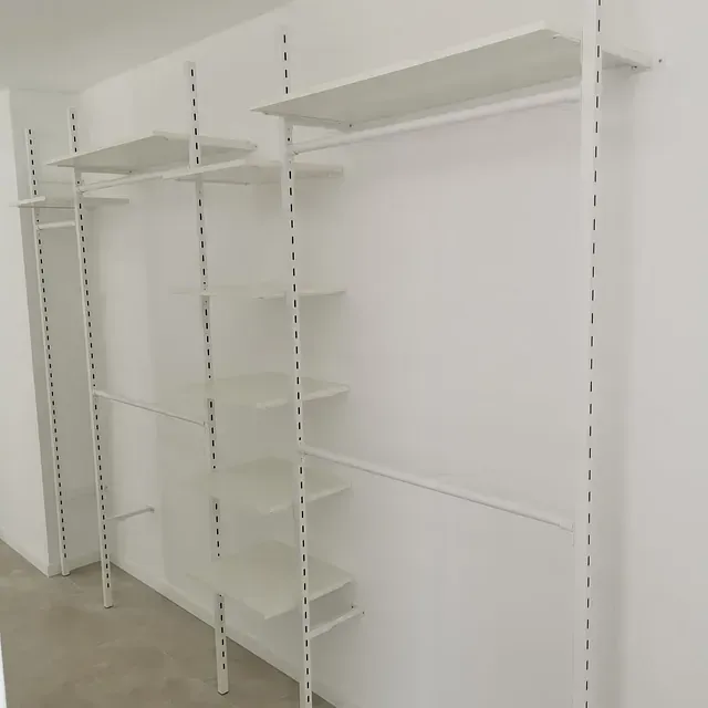 Un vestidor con estantes blancos y percheros.