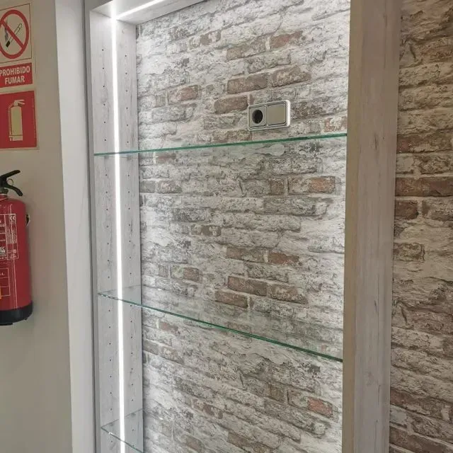 Una pared de ladrillos con un estante de vidrio y un extintor de incendios.