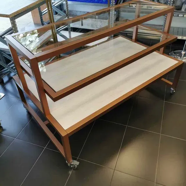 Una mesa de madera con tres estantes y una tapa de cristal.