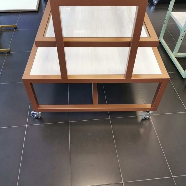 Una mesa de madera con ruedas se encuentra sobre un suelo de baldosas.