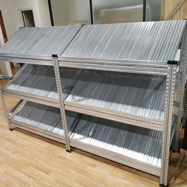 Un estante de metal con tres estantes está sobre un piso de madera.