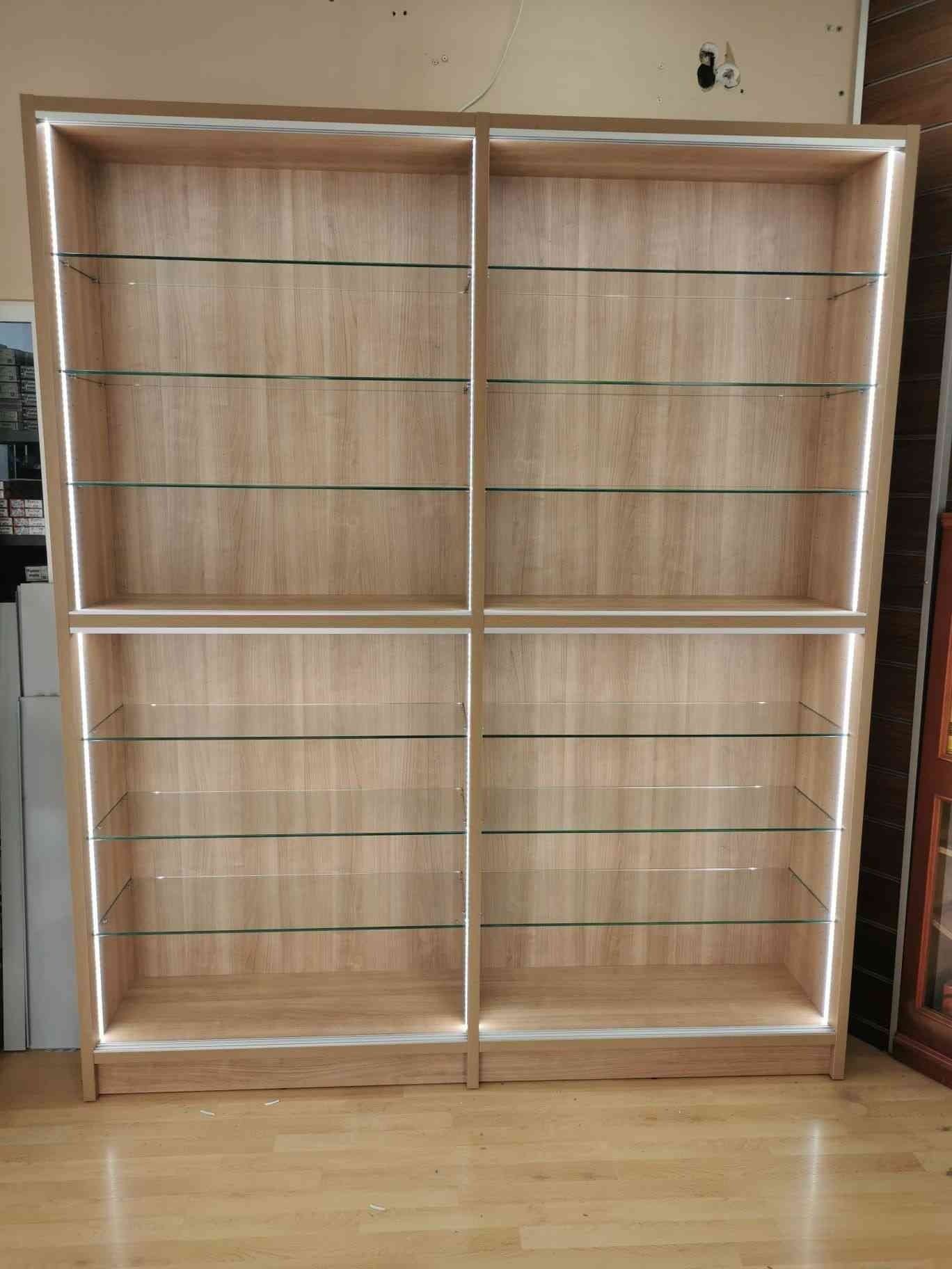 Un estante de madera con estantes de vidrio y luces está sobre un piso de madera.