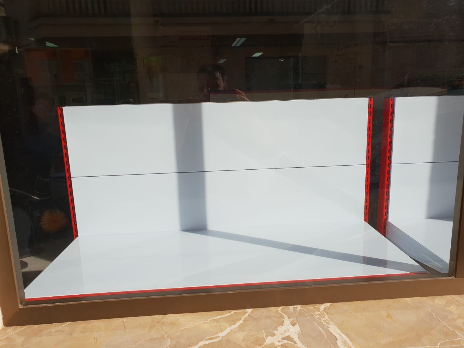 Una caja blanca con un borde rojo se encuentra dentro de una vitrina de cristal.