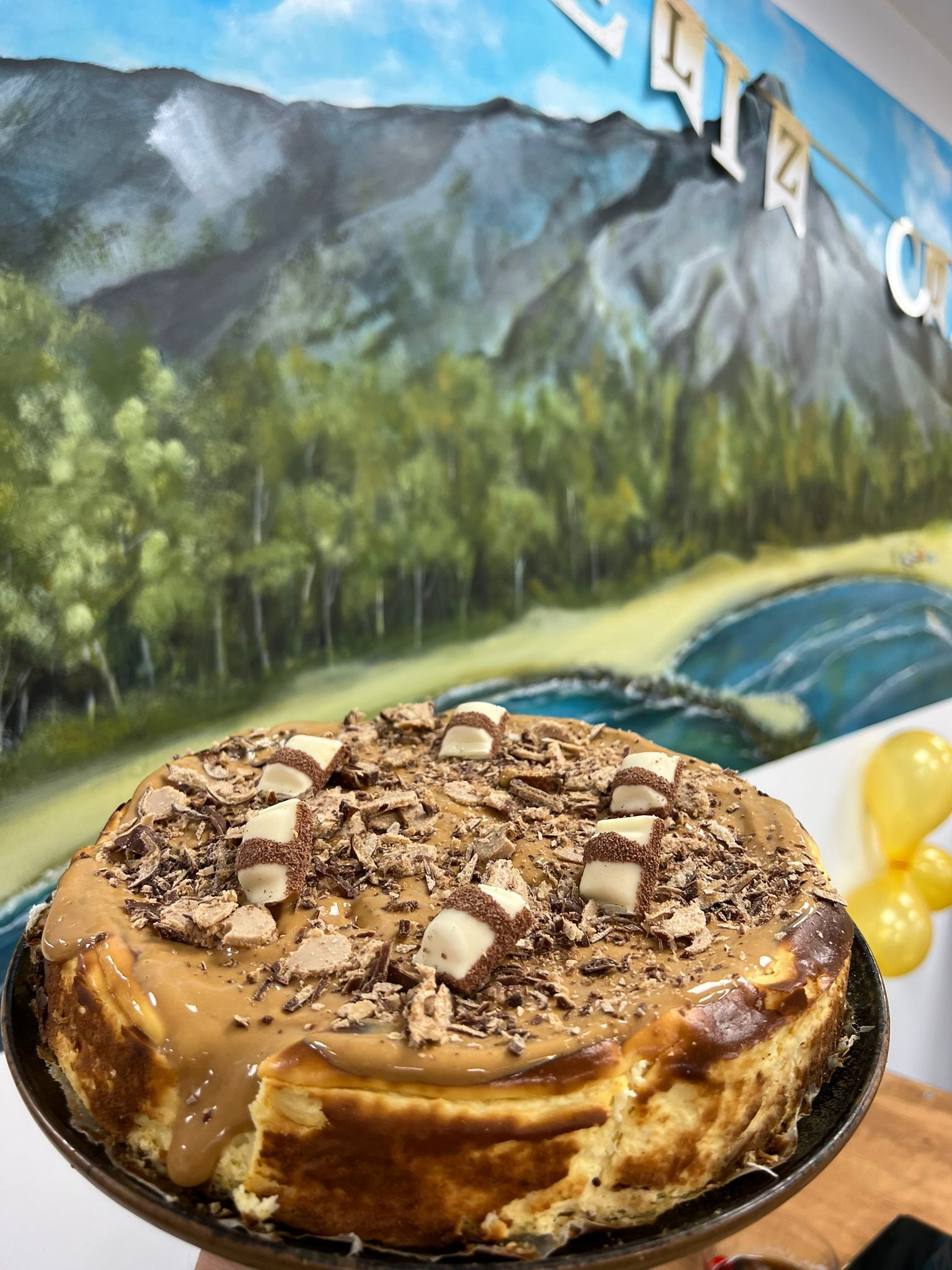 Una tarta de queso reposa en un plato delante de un cuadro de montañas.