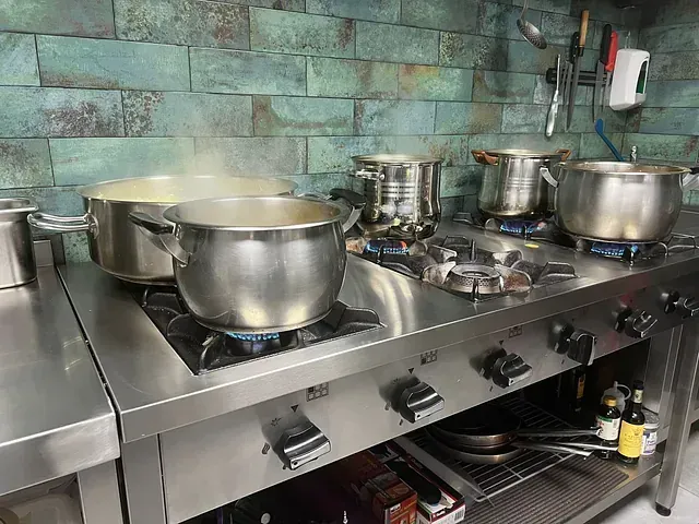 Una cocina con ollas y sartenes cocinando en una estufa.