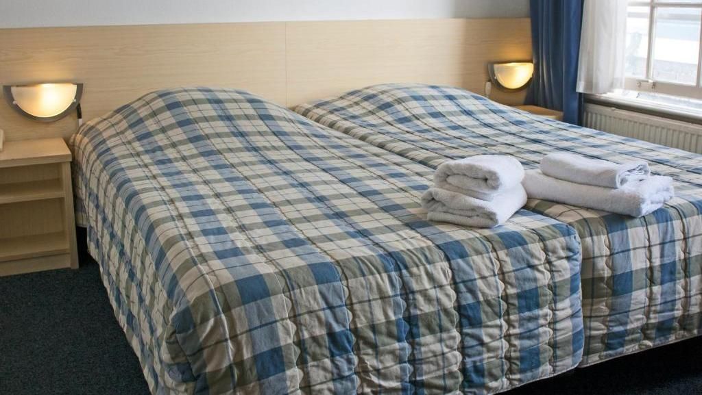 Two twin beds with blue plaid comforters in a hotel room, topped with white towels.