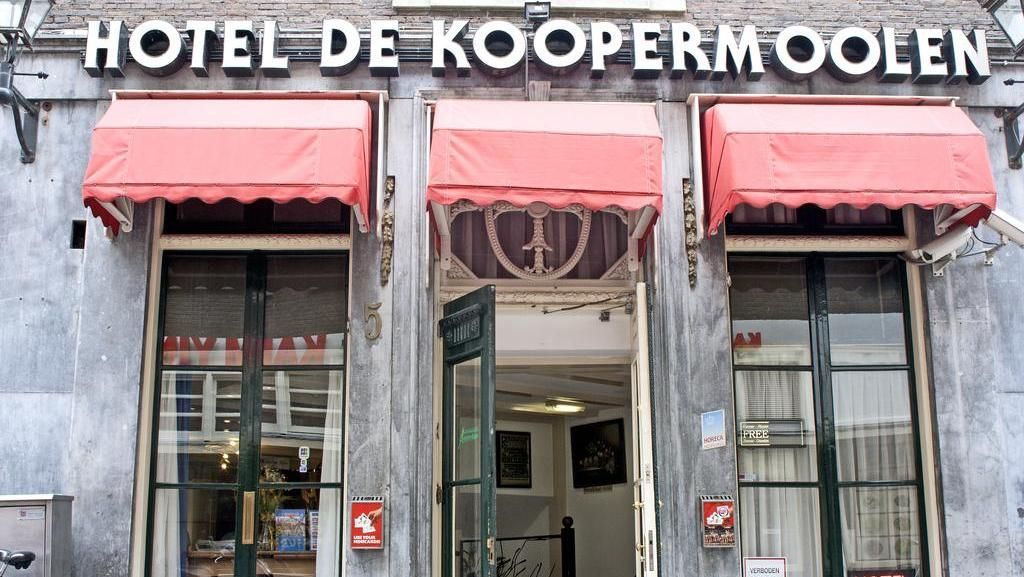 Hotel De Koopermoolen building exterior with red awnings over doors and windows. Gray facade with white text.