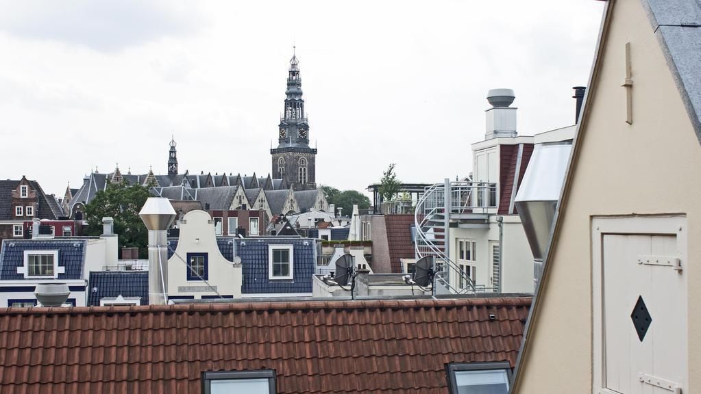 Rooftop view of Amsterdam buildings with distinctive gabled architecture and a prominent church spire against a cloudy sky.