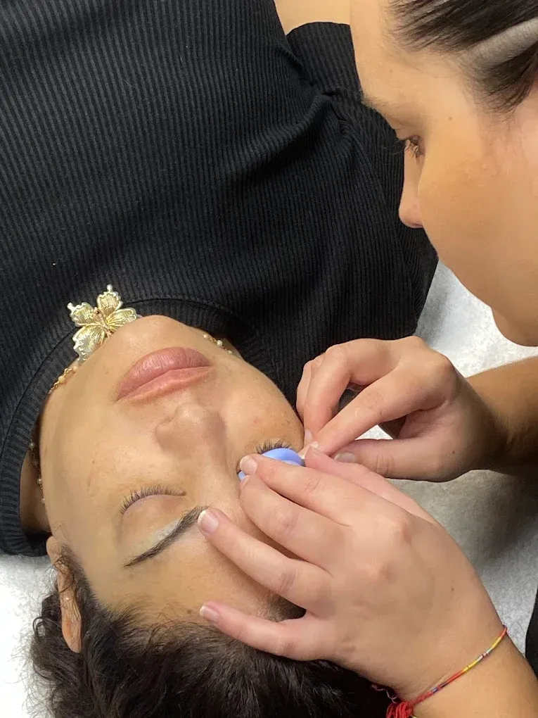 Una mujer está acostada en una cama mientras le arreglan las pestañas.