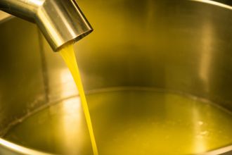 Aceite de oliva vertido desde un pico metálico en un recipiente de acero inoxidable.