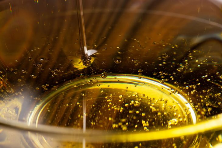 Aceite vertido en un vaso transparente, mostrando burbujas y un color dorado.