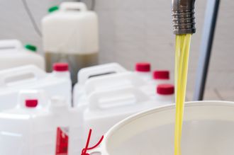 Líquido amarillo que sale de un grifo hacia un recipiente; recipientes de plástico blancos en el fondo.