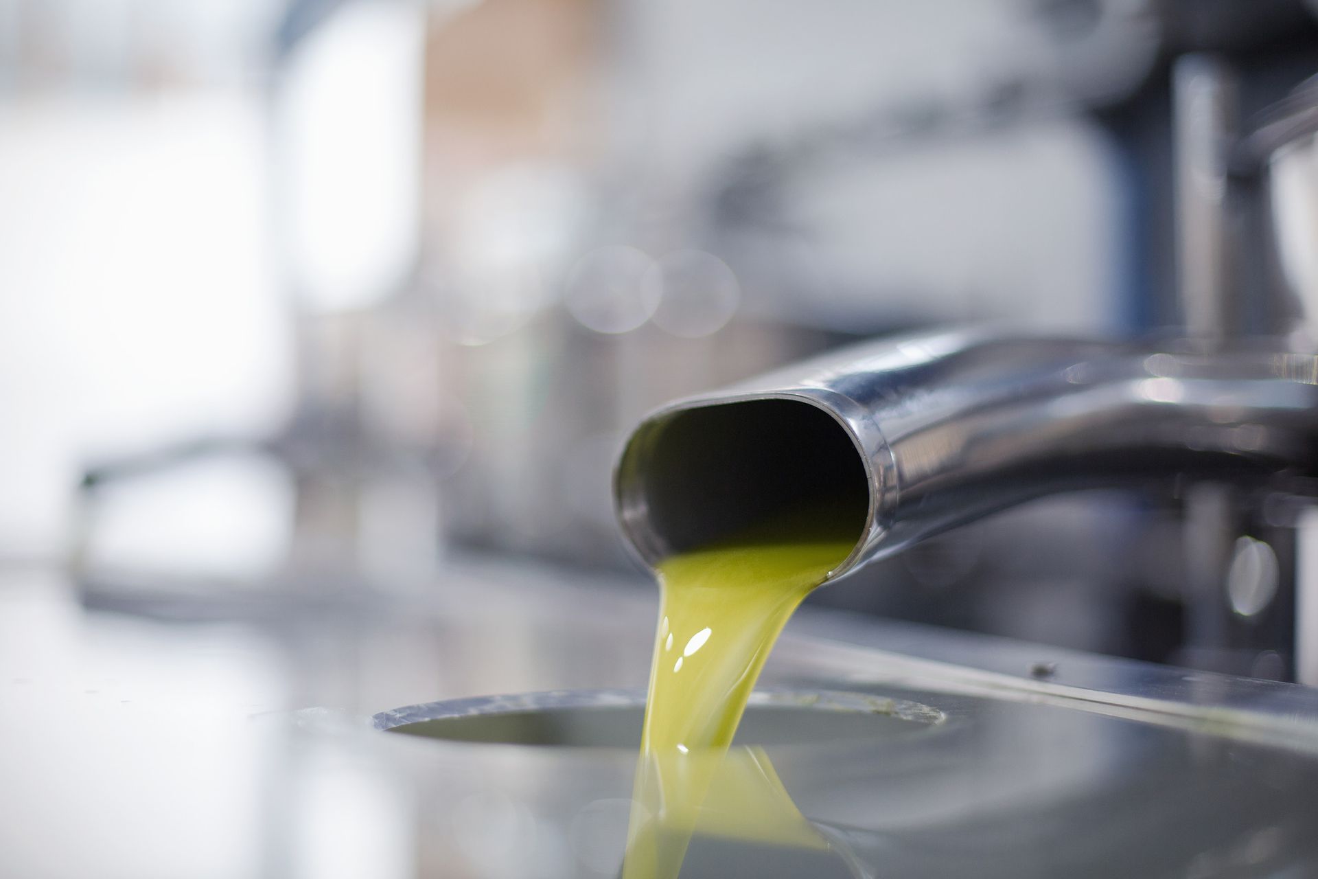 Aceite de oliva vertiéndose desde un pico de acero inoxidable en un recipiente, toma de primer plano.