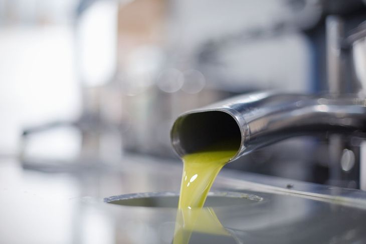 Aceite de oliva vertiéndose desde un pico de acero inoxidable en un recipiente, toma de primer plano.