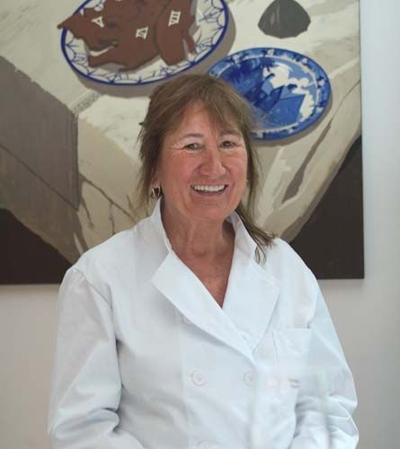 Una mujer con bata blanca sonríe delante de un cuadro.