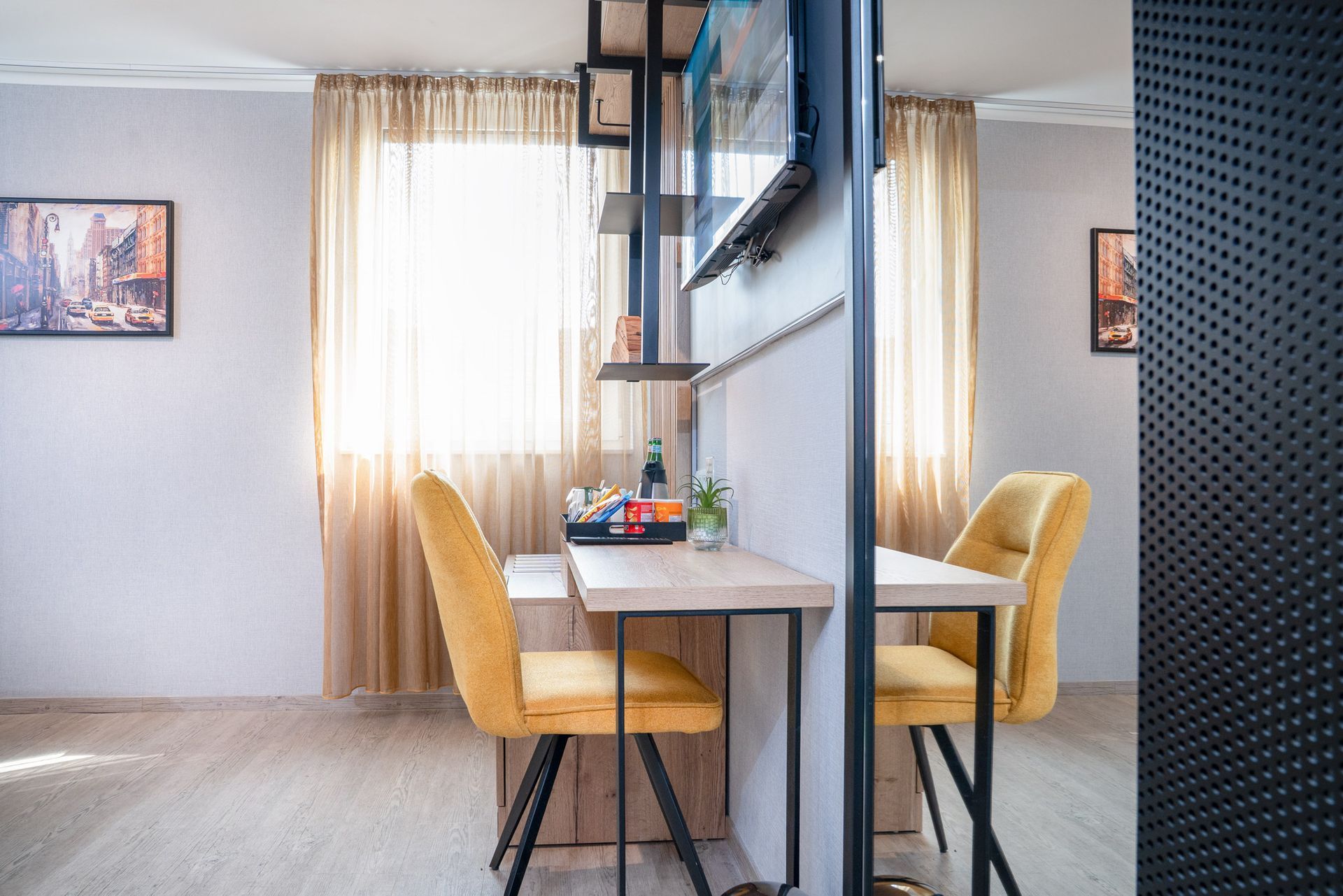 Essbereich mit Tisch und zwei gelben Stühlen; Raumteiler; hellbeige Vorhänge.