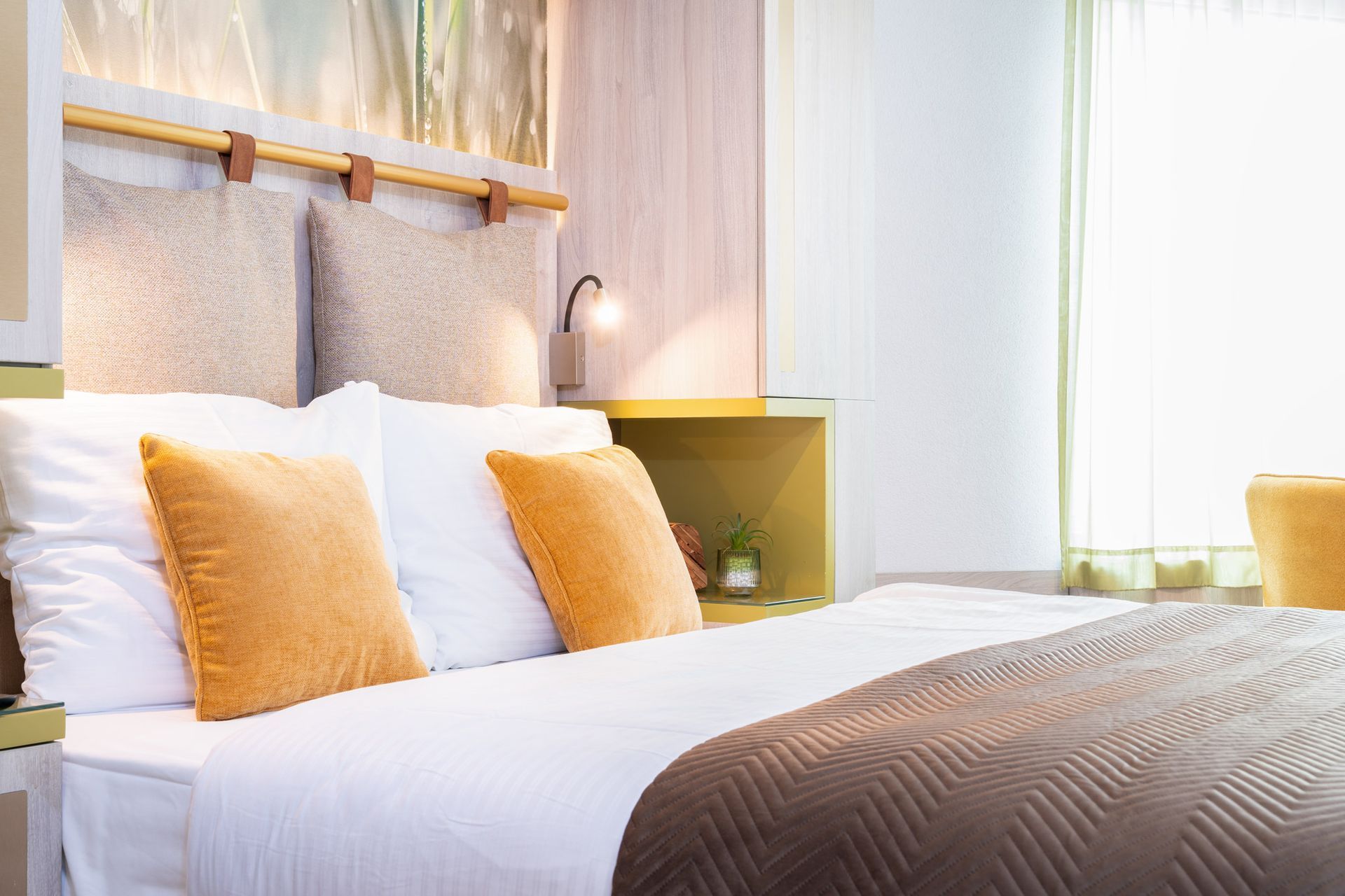 Schlafzimmer mit einem Bett, bezogen mit weißer Bettwäsche und braunen und orangefarbenen Kissen.