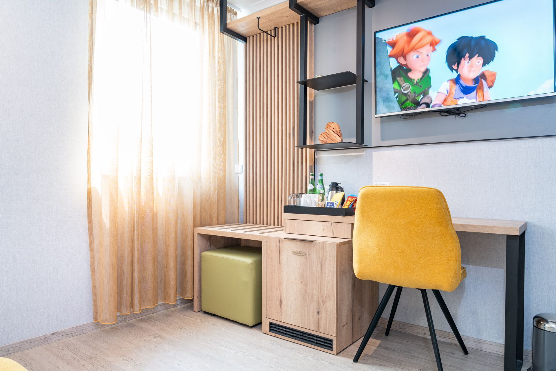 Ein Hotelzimmer mit Schreibtisch, Stuhl, Fernseher und Fenster mit Vorhängen; auf dem Fernsehbildschirm