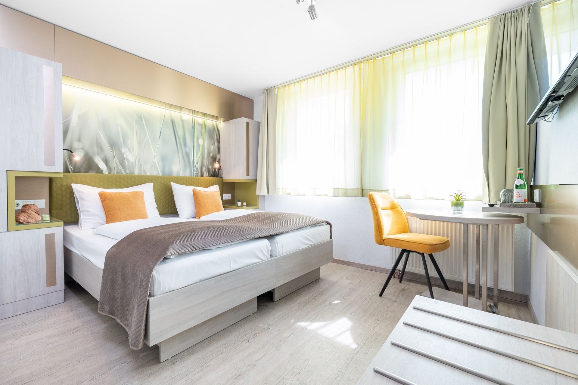 Hotelzimmer mit Doppelbett, gelbem Sessel und Fenster mit Vorhängen.