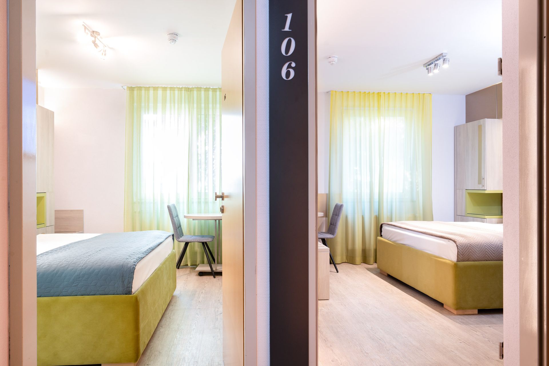 Zwei Hotelzimmer, die Türen sind geöffnet und geben den Blick frei auf ein Bett, einen Schreibtisch und ein Fenster