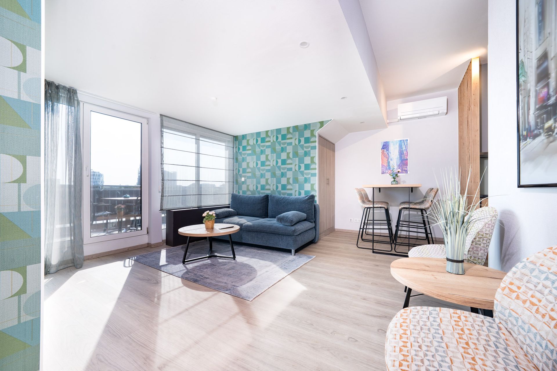 Helles Wohnzimmer mit blauem Sofa, hellem Holzboden und Balkon. Türkisfarbene Akzentwand mit Muster.