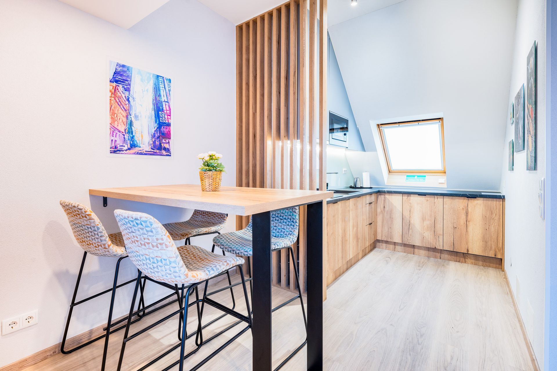 Kochnische mit Holzschränken und einem Tisch mit Stühlen; Kunstwerke an der Wand.