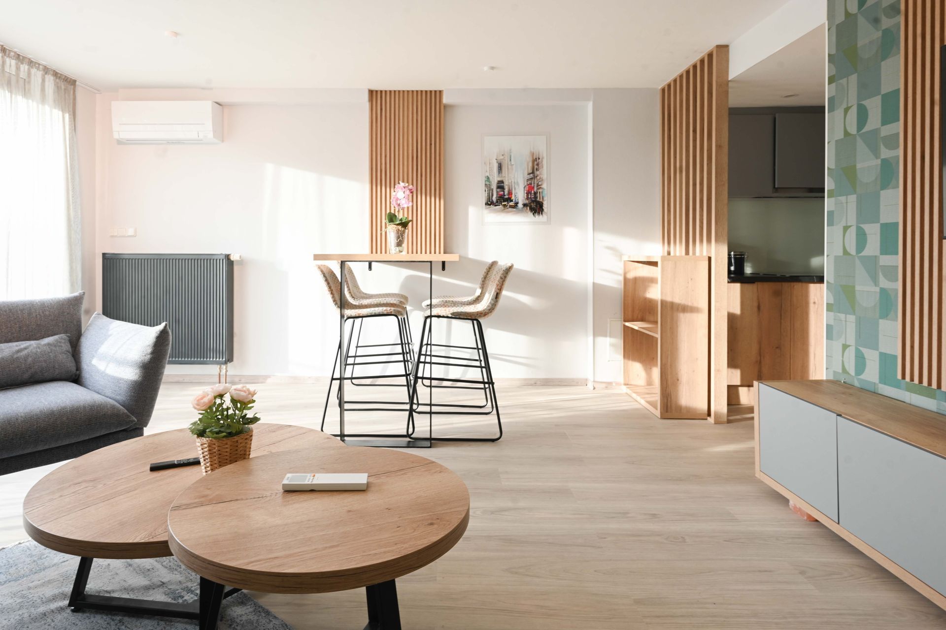 Gemütliches Wohnzimmer mit Holzelementen, grauem Sofa, zwei runden Couchtischen und einer Frühstücksbar.