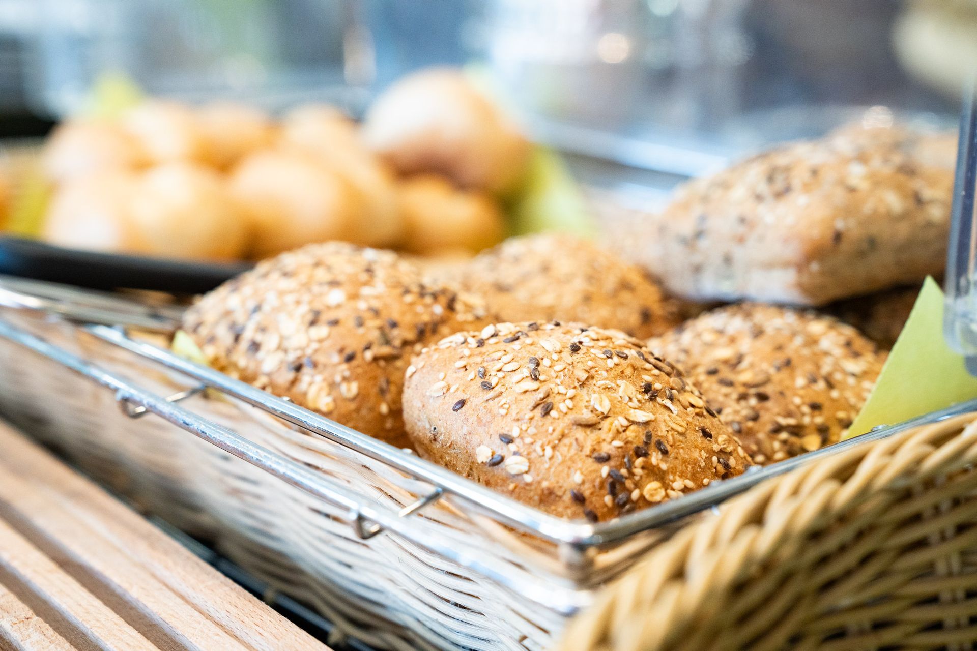 Ein Korb mit Körnerbrötchen, Nahaufnahme; im Hintergrund sind andere Backwaren unscharf zu sehen.