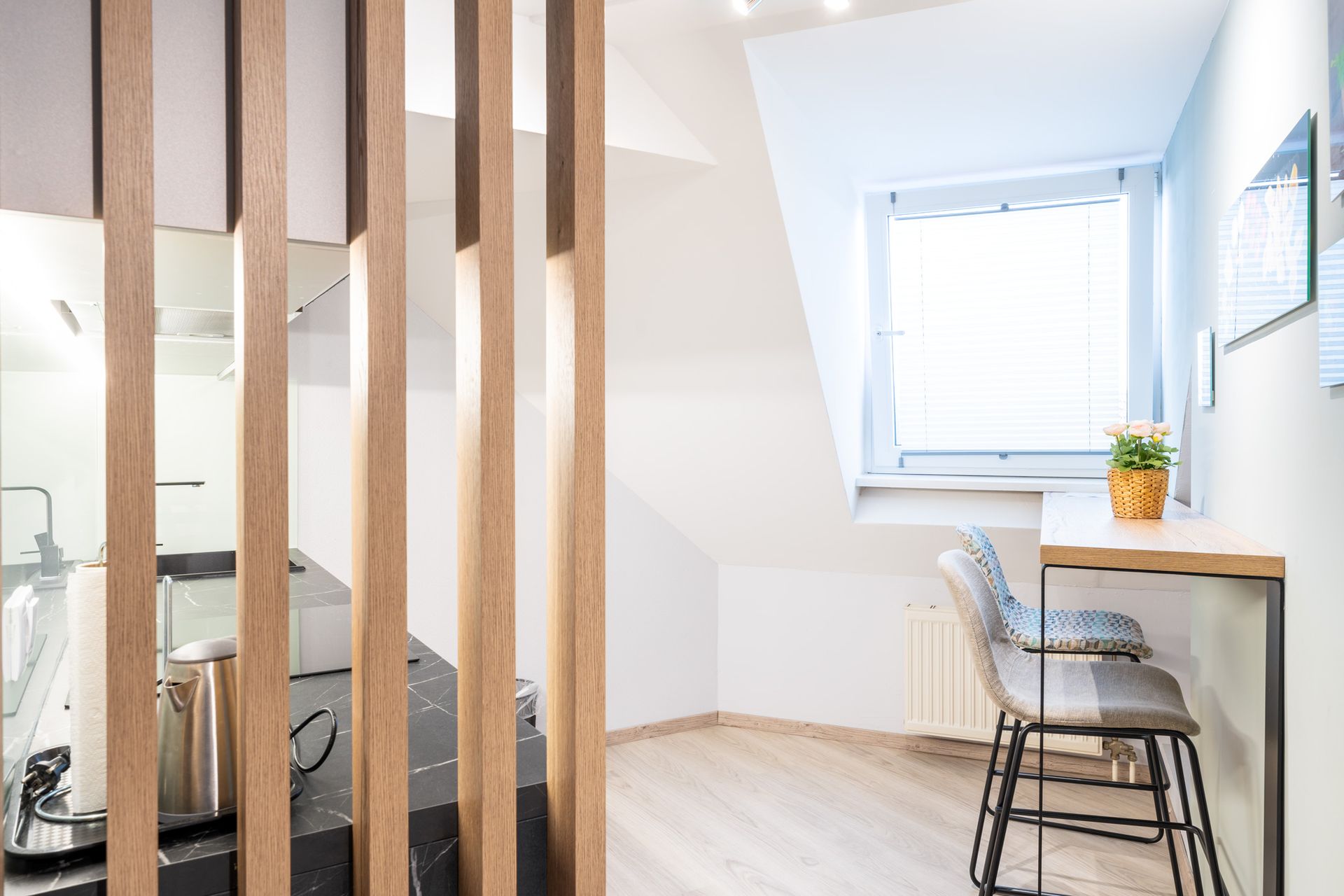 Raumteiler aus Holzlatten trennt die Küche vom Schreibtisch am Fenster.