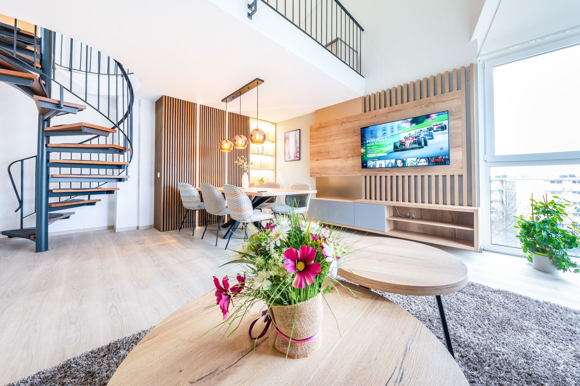 Modernes Loft-Interieur mit Wendeltreppe, Essbereich und floralem Mittelstück.