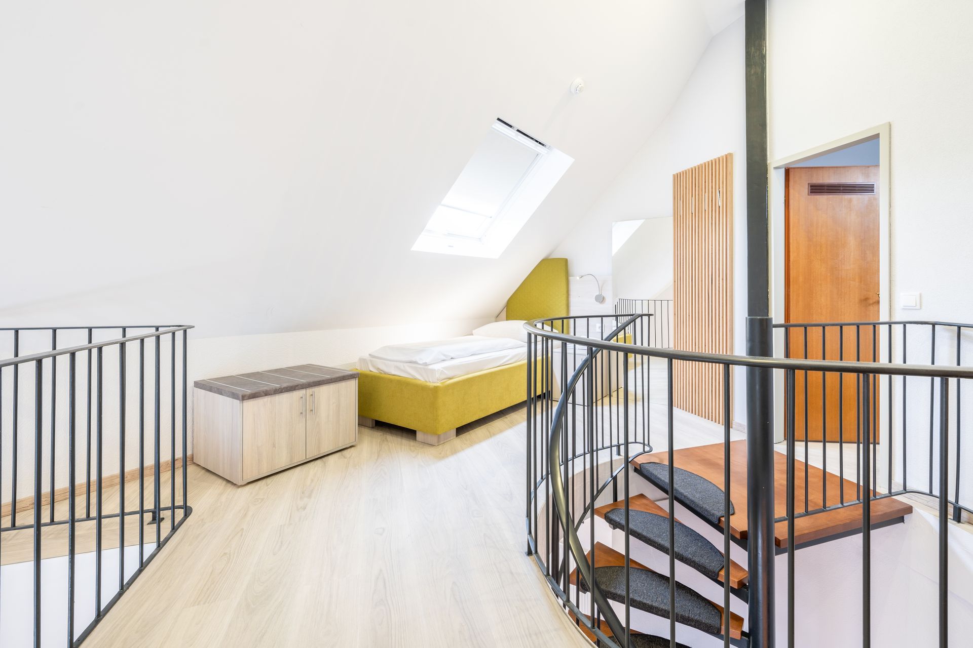 Loft-Schlafzimmer mit Bett, Dachfenster, Wendeltreppe und Geländer. Helle, weiße Wände und helle Holzböden.
