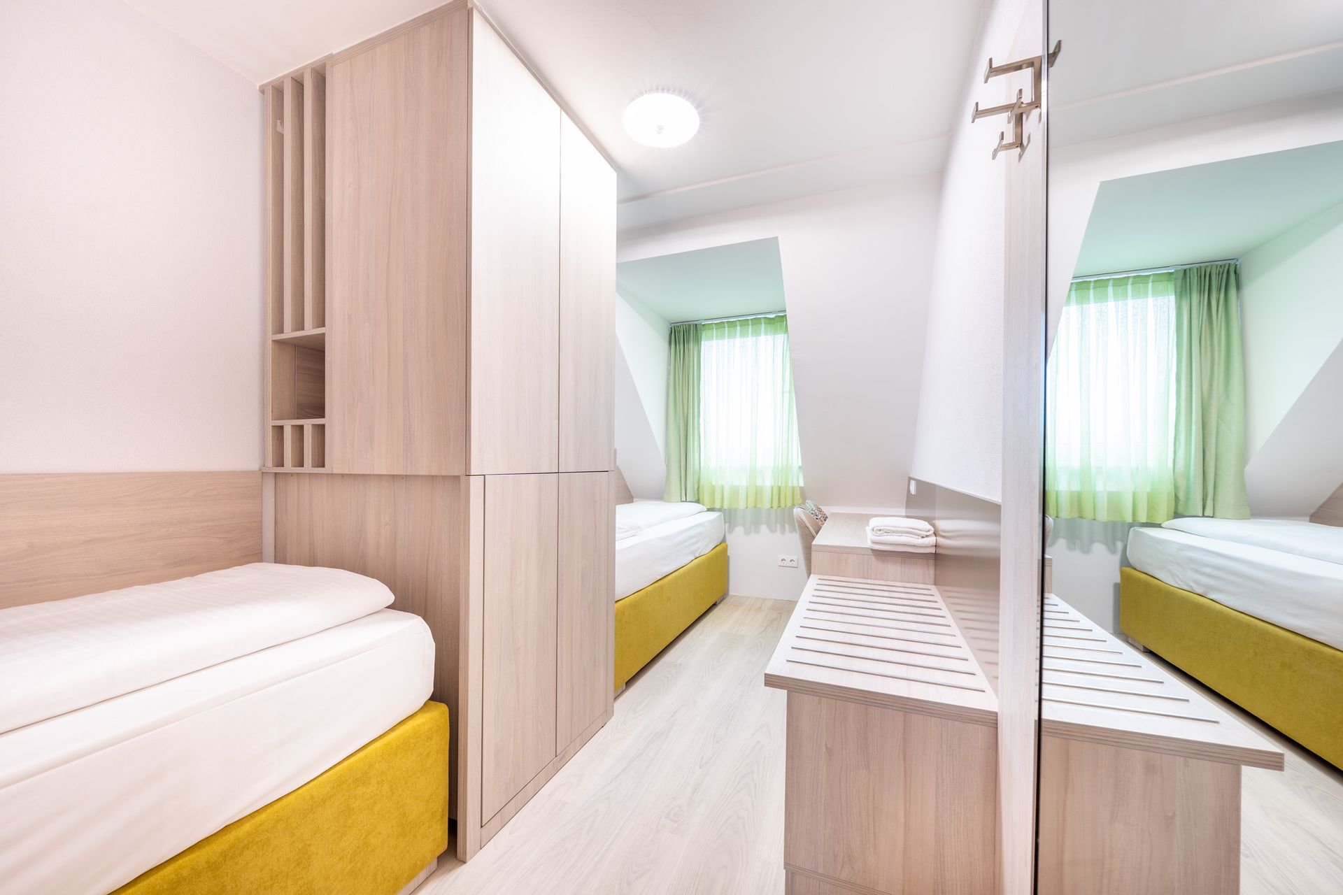 Schmale Schlafzimmertür mit zwei Einzelbetten, Kleiderschrank und Spiegel, in dem sich das Bett reflektiert