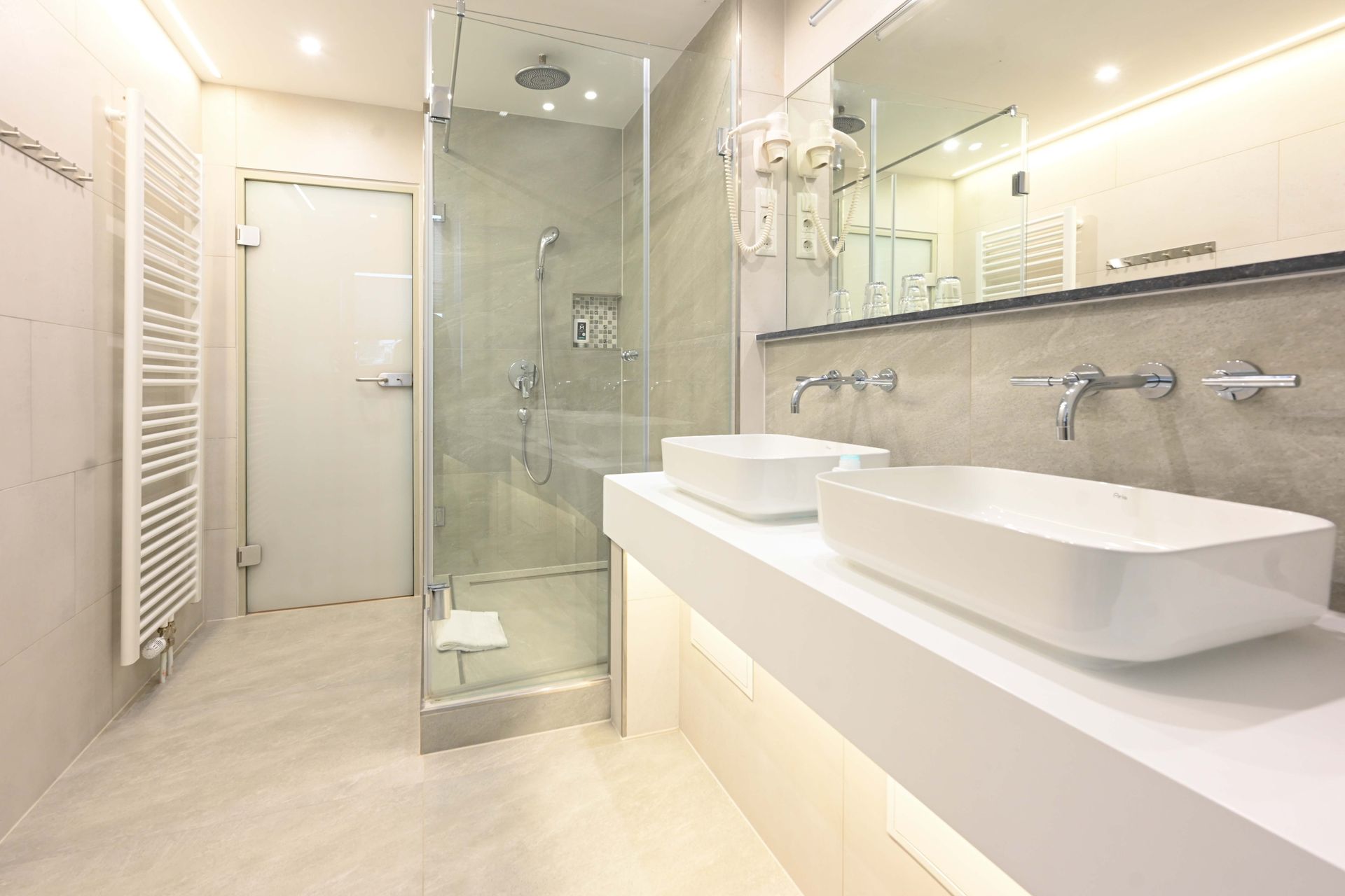 Modernes Badezimmer mit Glasdusche, Doppelwaschbecken, großem Spiegel und beheiztem Handtuchhalter.