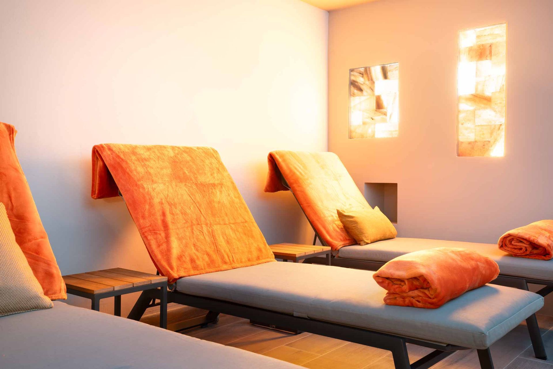 Ruheraum mit Liegestühlen, orangefarbenen Handtüchern und beleuchteten Salzpaneelen.