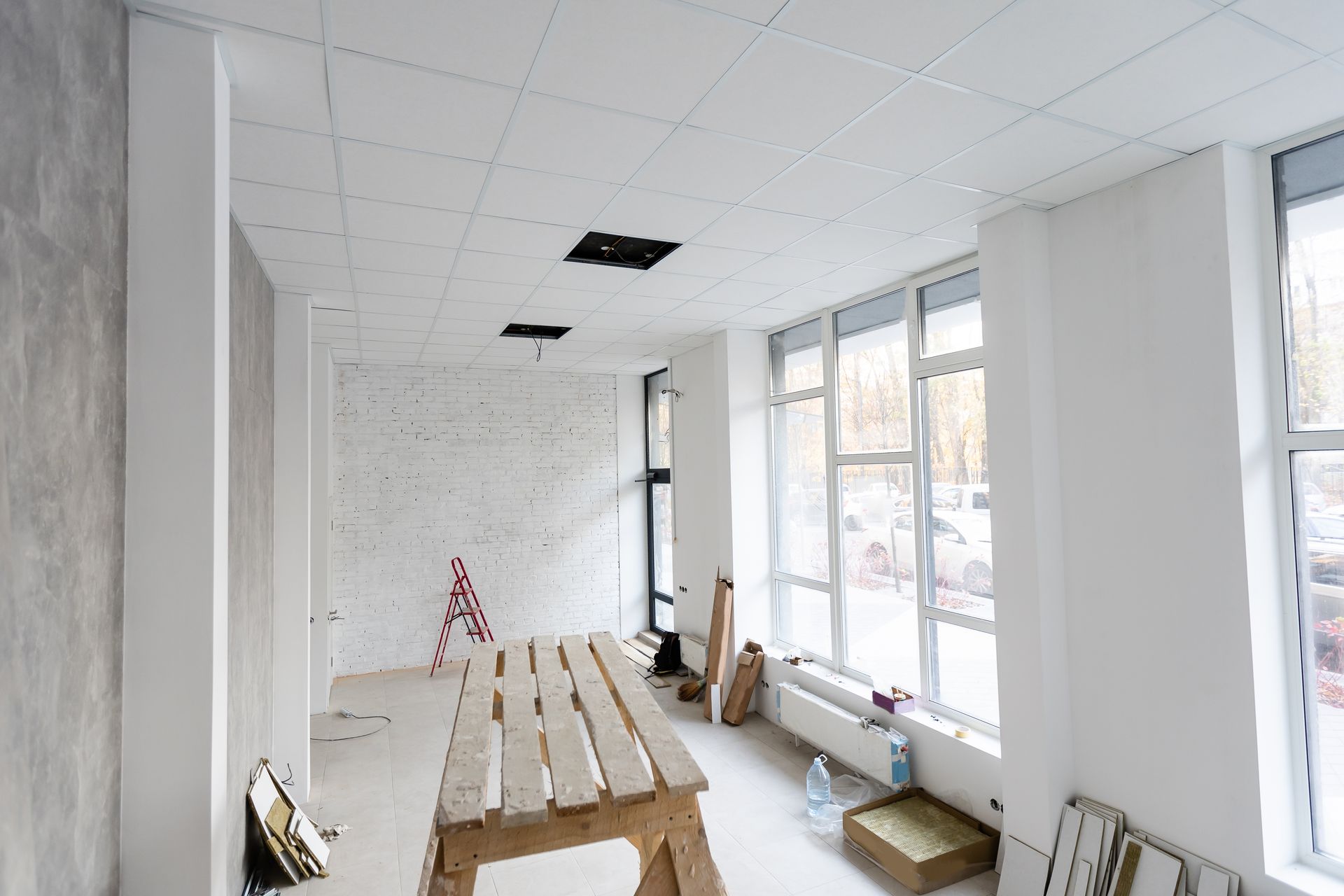 Une pièce inachevée en cours de rénovation, avec des murs, un plafond à caissons, de grandes fenêtres et un établi en bois.