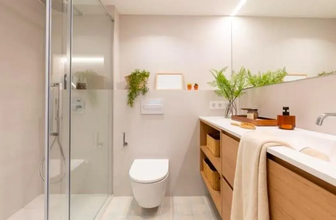 Baño moderno con ducha de cristal, inodoro suspendido y tocador de madera con plantas.