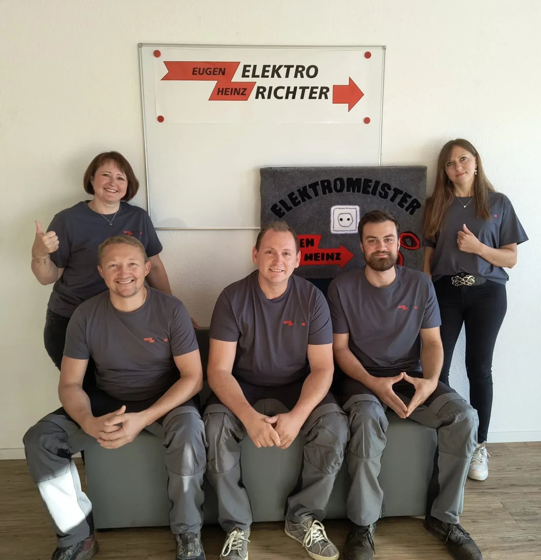 Sechs Personen in einheitlichen grauen Hemden posieren drinnen vor einem Elektro RICHTER-Schild.