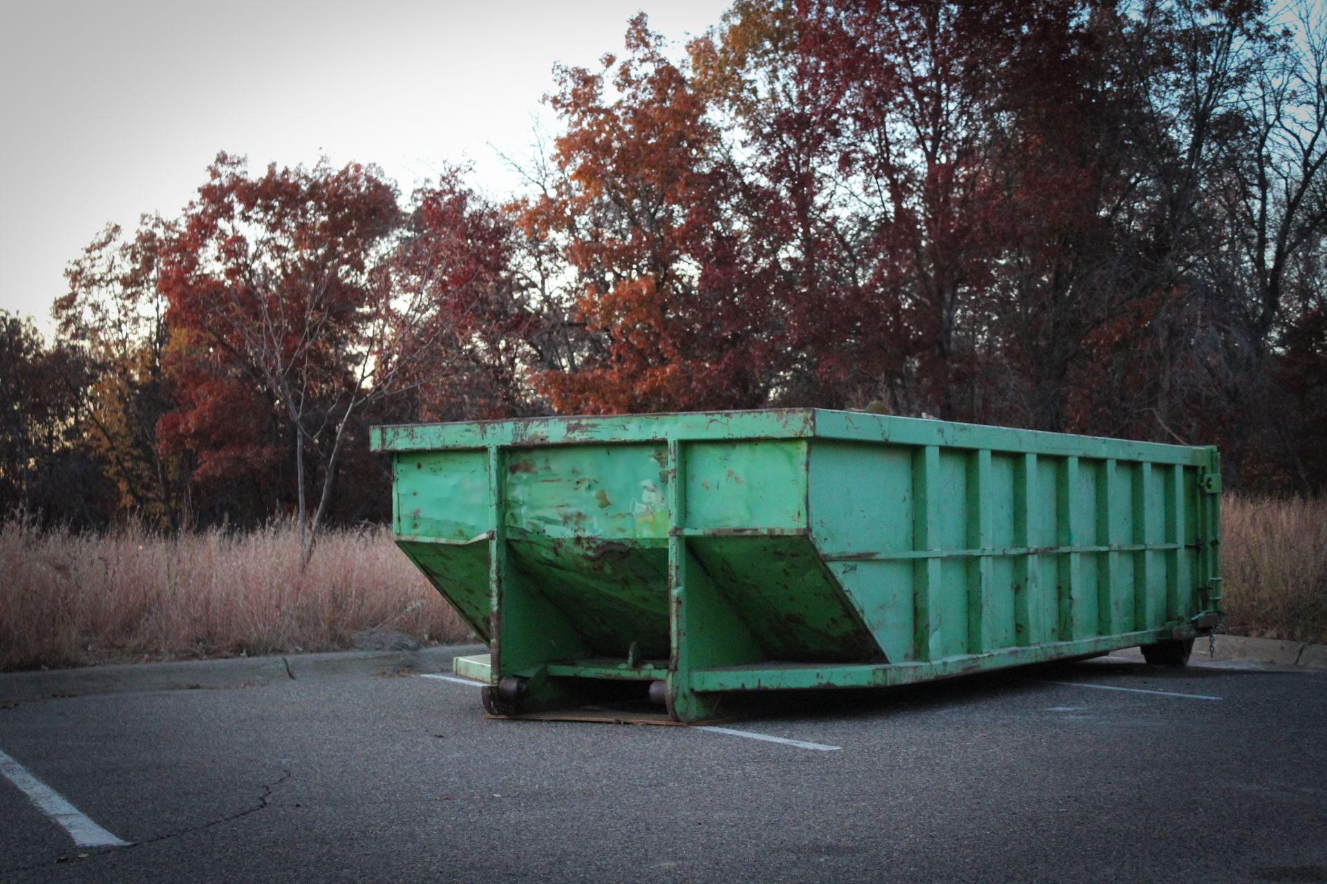 Benne à déchets verte posée sur un stationnement vide.
