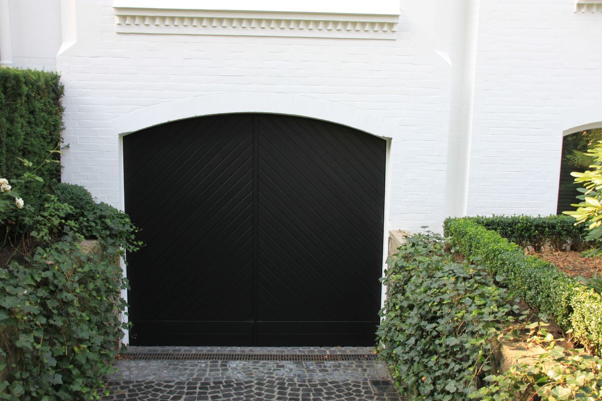 Vor einem weißen Backsteingebäude steht ein schwarzes Garagentor.