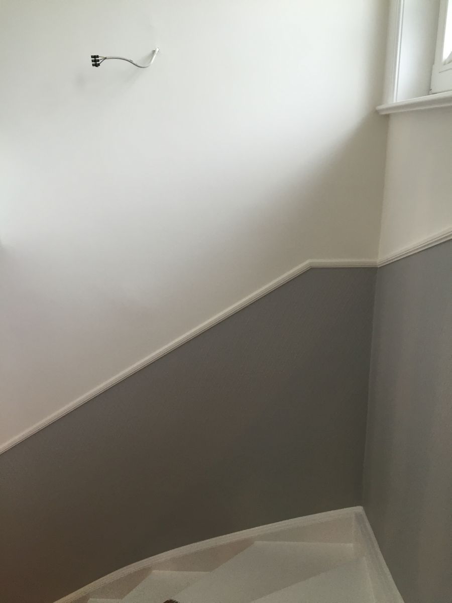 In einem Badezimmer wird eine weiße Wand mit grauer Zierleiste gestrichen.