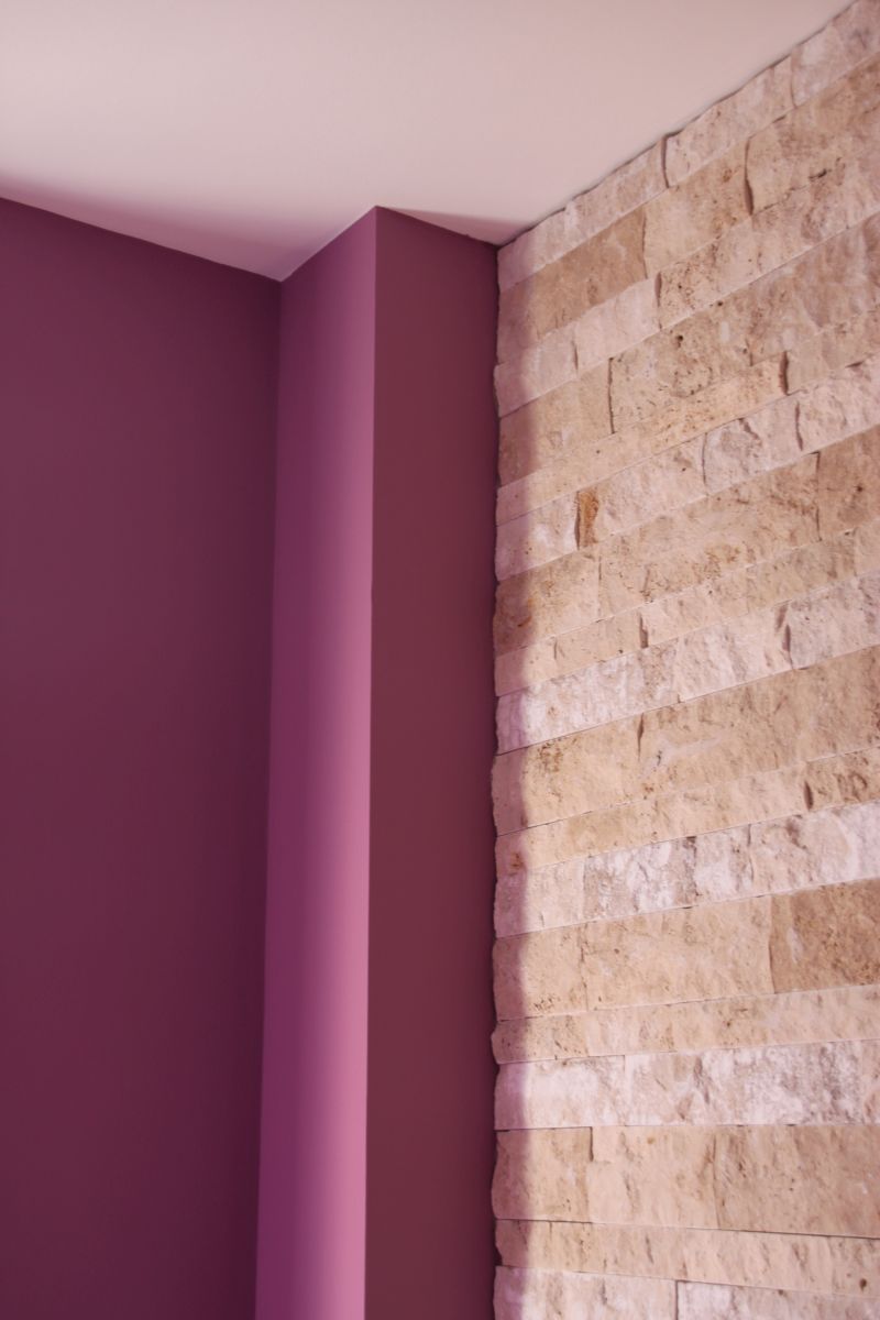Eine Zimmerecke mit violetten Wänden und einer Ziegelwand.