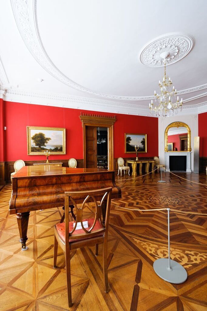 In einem Raum mit roten Wänden und Holzboden steht ein Klavier.