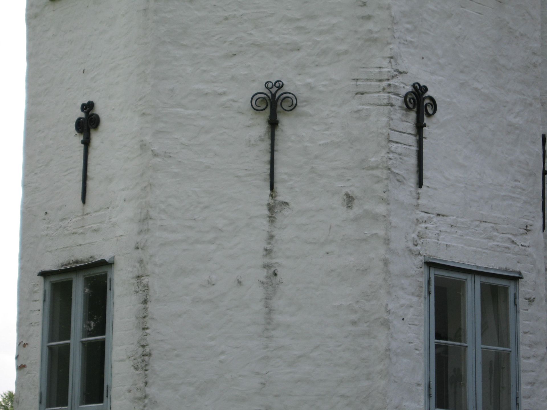 Ein weißes Backsteingebäude mit drei Fenstern und einem Kreuz an der Seite