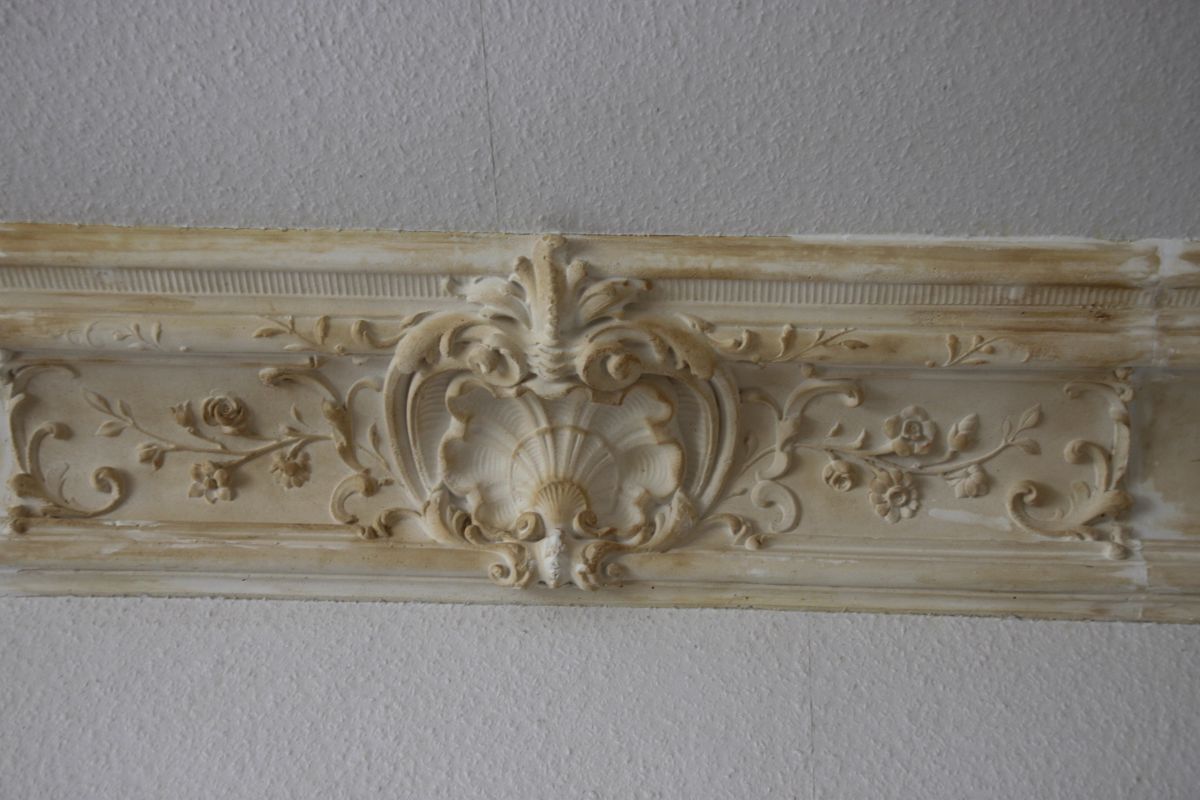 An einer weißen Wand hängt ein weißes Gesims mit Blumenmuster.