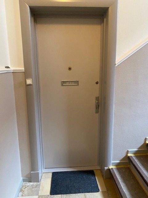 Eine Tür in einem Flur mit Treppe und einer Matte auf dem Boden.