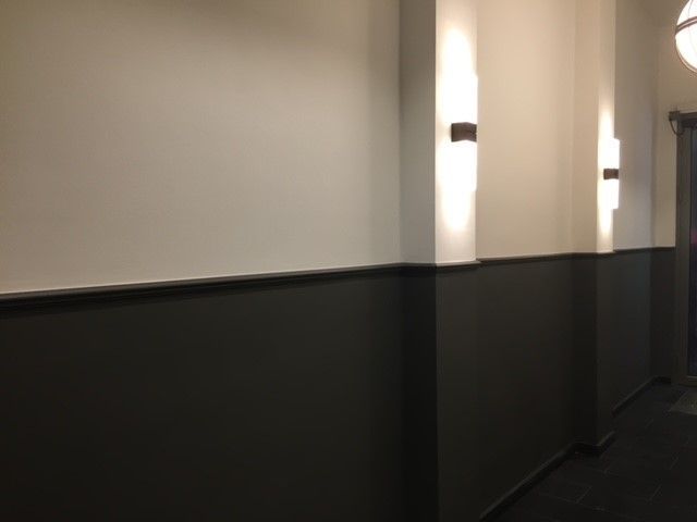 Ein langer Flur mit schwarzen und weißen Wänden und einer Lampe an der Wand.