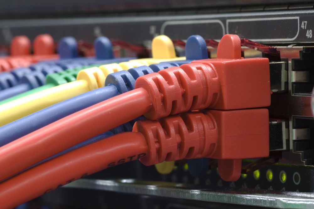 Primer plano de cables Ethernet de colores conectados a un conmutador de red, con cables rojo, azul y amarillo visibles.