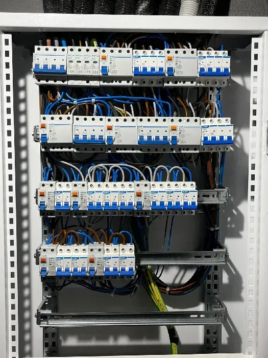 Panel eléctrico con filas de disyuntores y cableado, predominantemente cables azules y marrones.